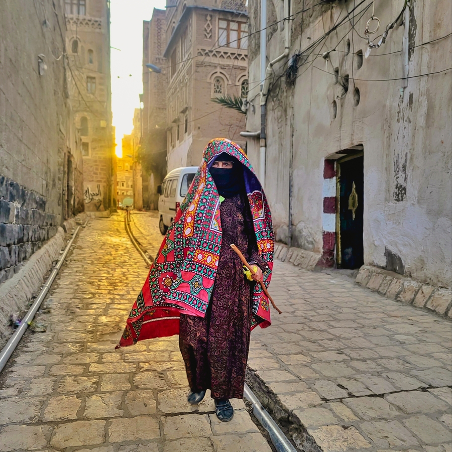 a woman walking down a street in the old city of Old Sanaa