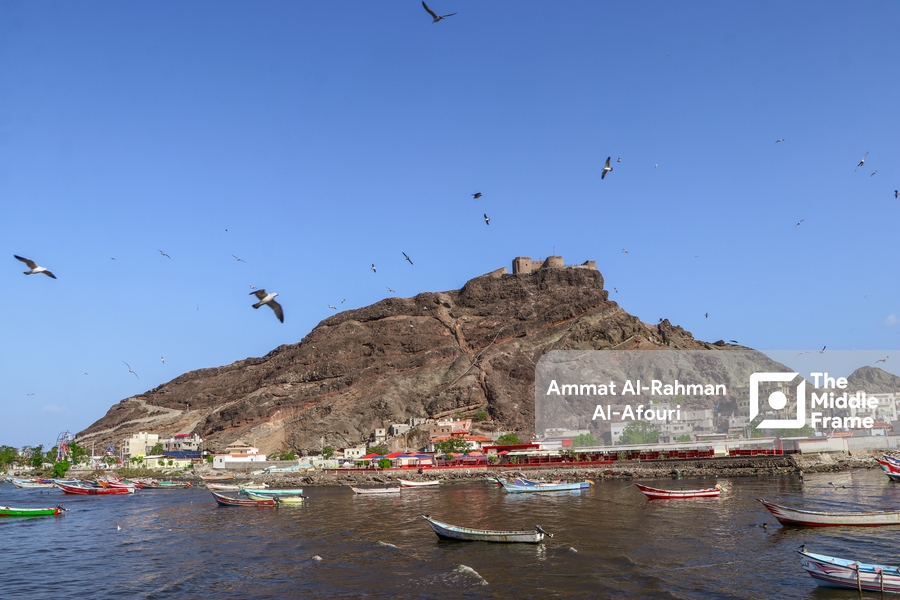 A beautiful scene of a volcanic island with the birds flying under a clear sky and small fishing boats anchored in the harbor