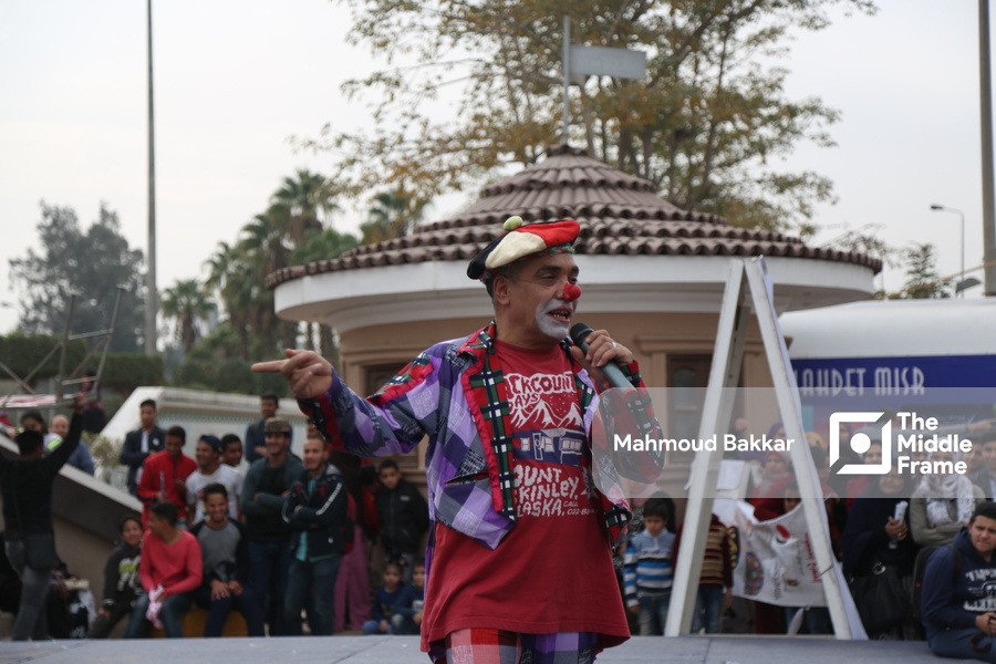An old man dressed as a clown performs in front of an audience.