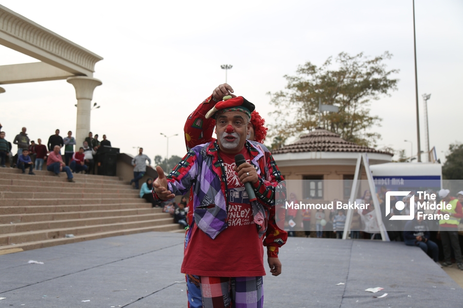 An old man dressed as a clown performs in front of an audience.