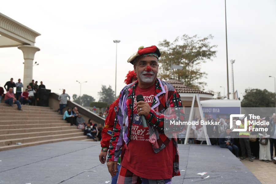 An old man dressed as a clown performs in front of an audience.