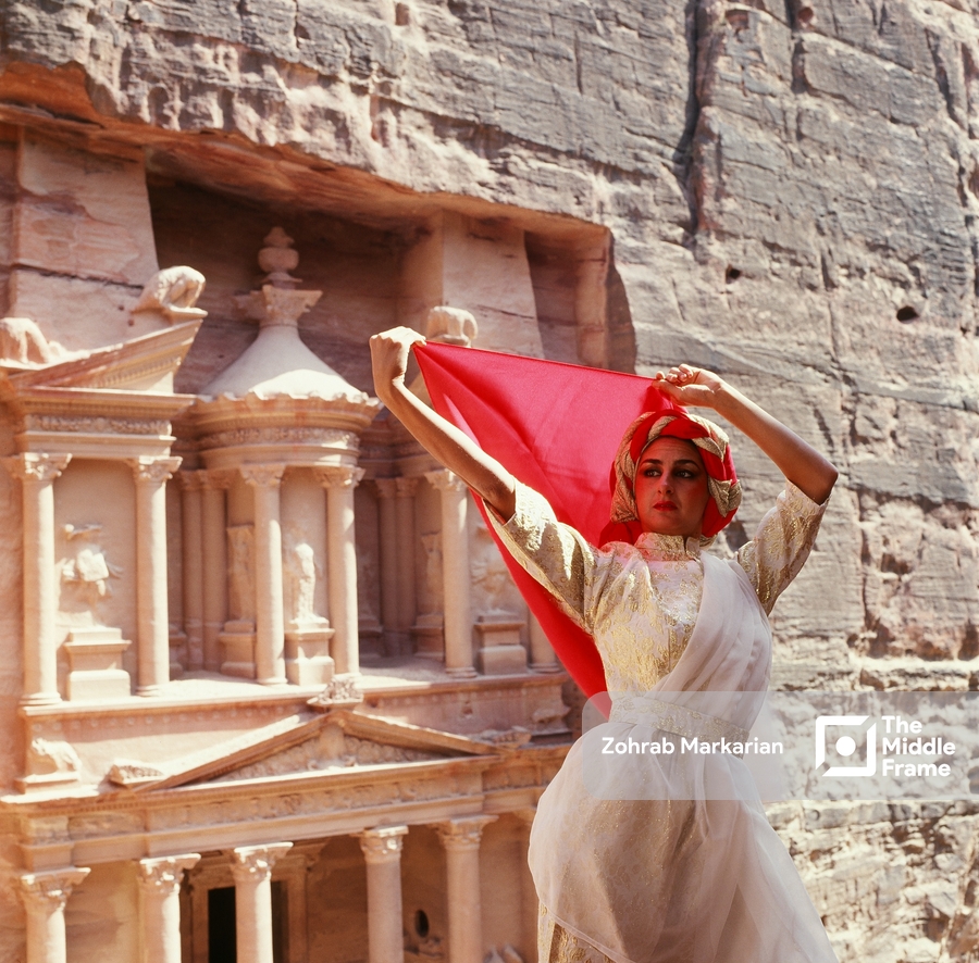 A woman in a white dress stands in front of a cliff