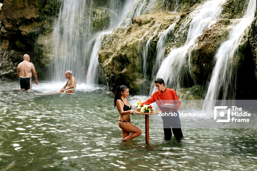 a man and woman are standing in the water near a waterfall
