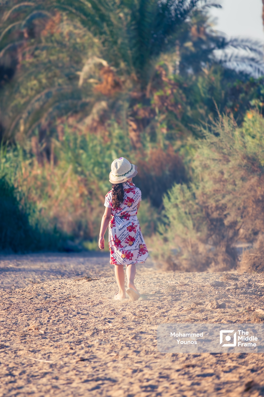 A little girl walks on the sand between the trees.