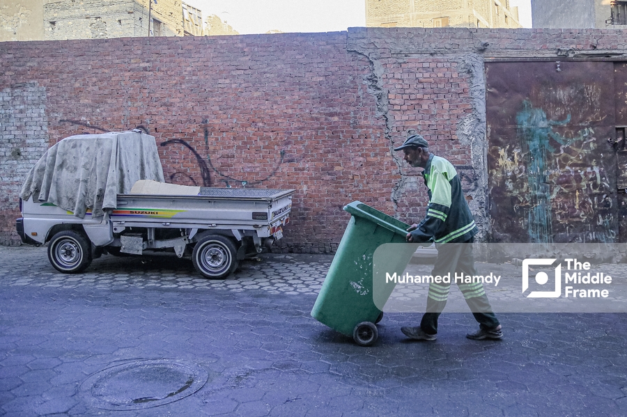 A cleaner in uniform pushing the trash bin down the street