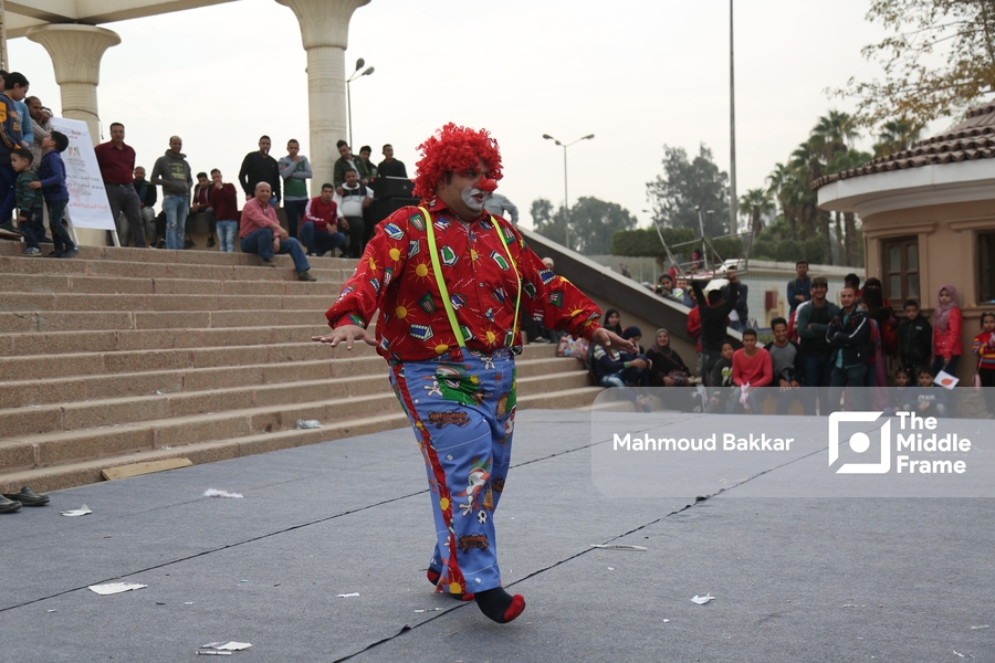 An old man dressed as a clown performs in front of an audience.