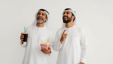 Two men in white clothes are holding a drink and a popcorn