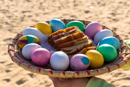 Close-Up of a Girl Holding a Round Basket with Colored Eggs and Cake Against the Desert Sands in Egypt
