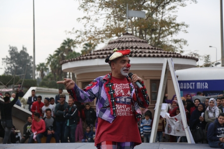An old man dressed as a clown performs in front of an audience.