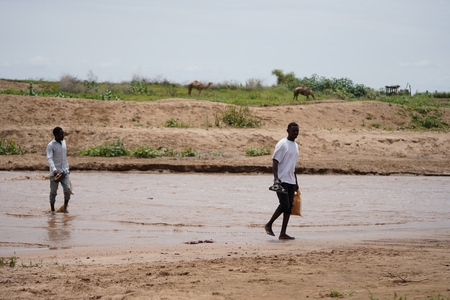 two men walking across a muddy river