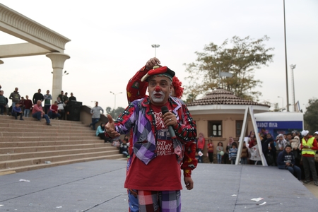 An old man dressed as a clown performs in front of an audience.