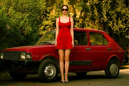 a woman in a red dress standing next to a red car