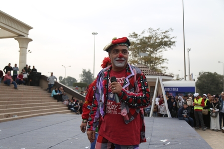 An old man dressed as a clown performs in front of an audience.