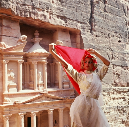 A woman in a white dress stands in front of a cliff