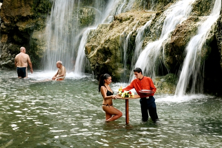 a man and woman are standing in the water near a waterfall