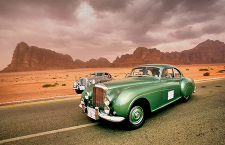a green car driving down the road in the desert