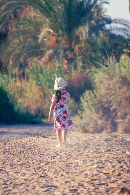 A little girl walks on the sand between the trees.