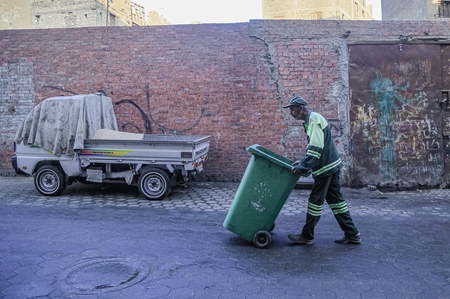 A cleaner in uniform pushing the trash bin down the street