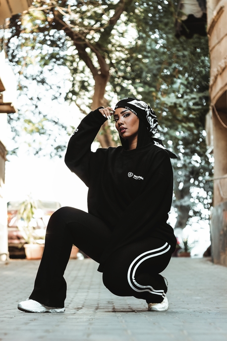 A young woman in a black outfit poses on the street in daylight in Egypt