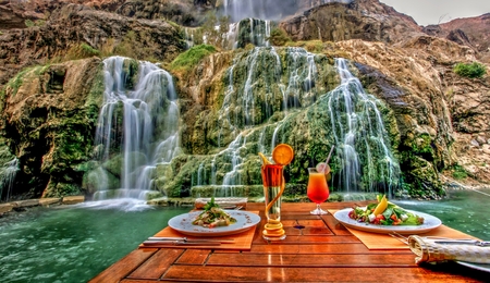a table with plates of food and a waterfall in the background