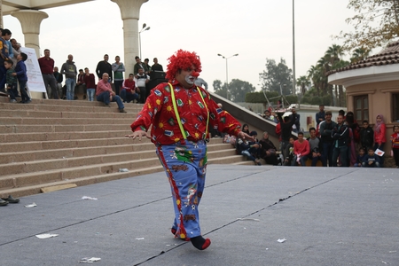 An old man dressed as a clown performs in front of an audience.
